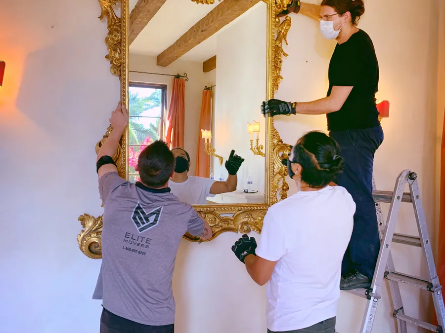 Three of the crew taking down a large gilded mirror